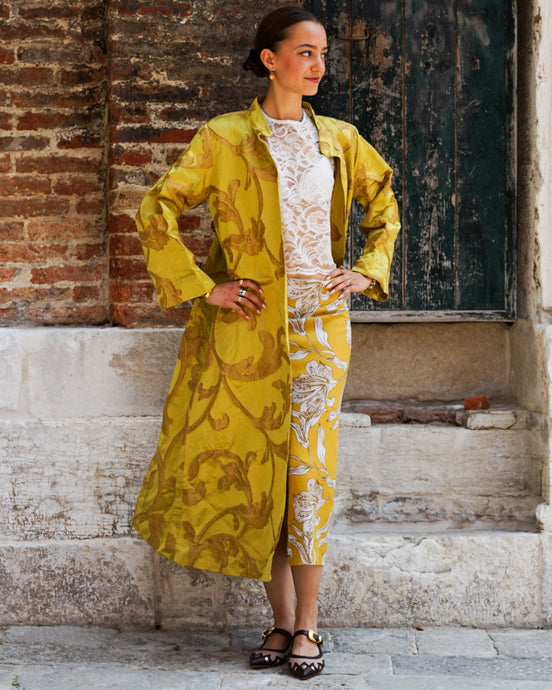 Woman wearing a yellow and white patterned outfit standing against a brick wall.